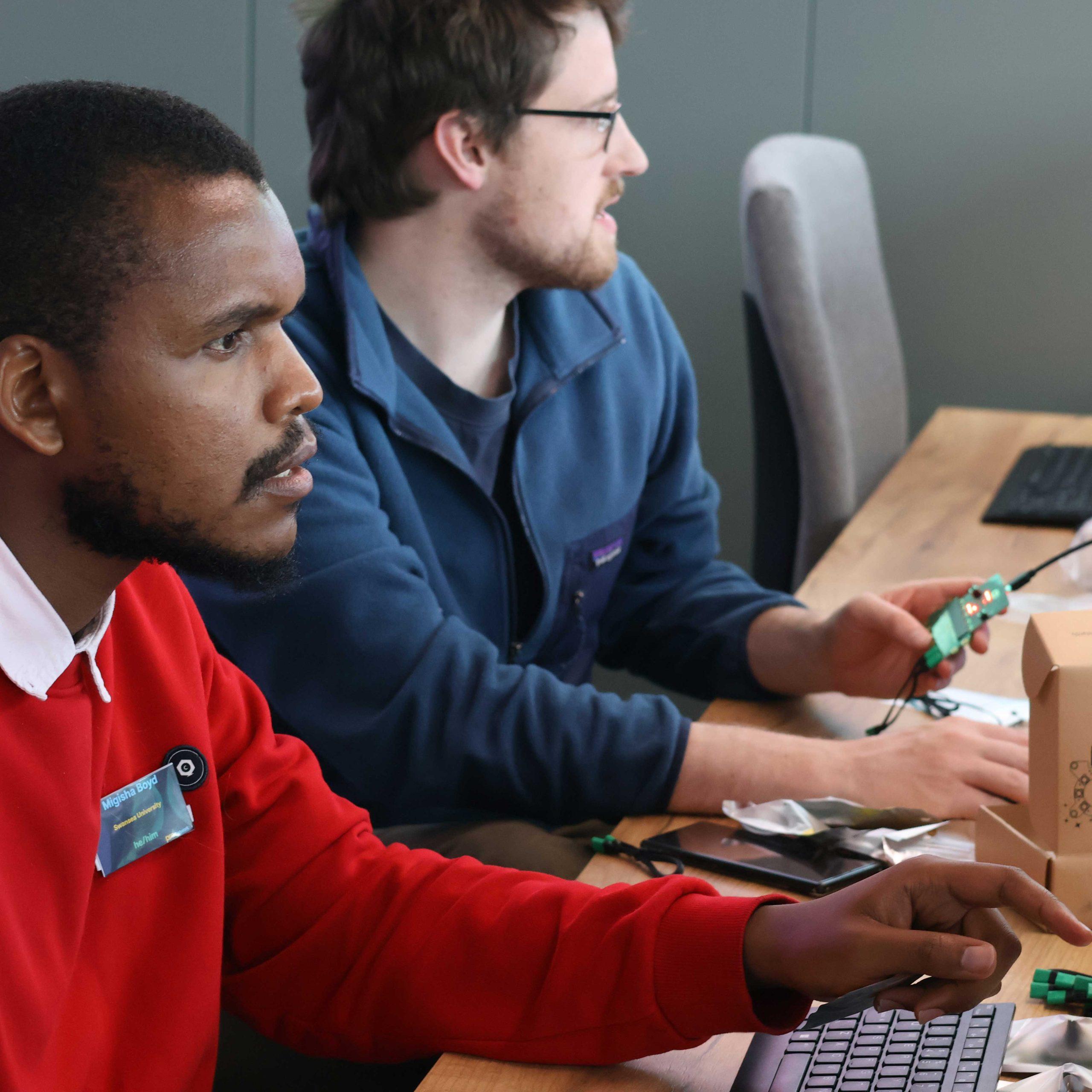 03 Two people sit in a computer lab holding electronics.