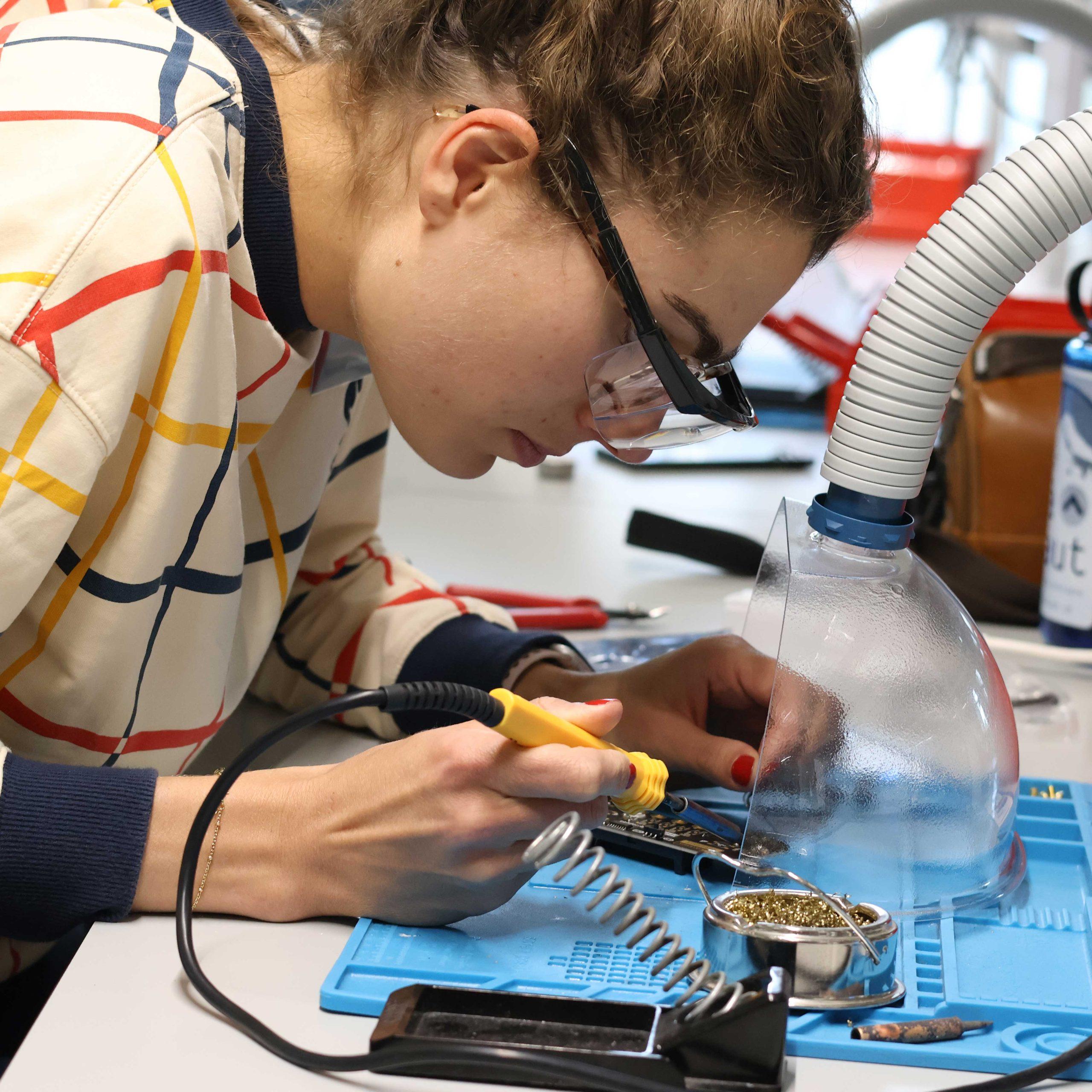 05 A person leans over a desk soldering a printed circuit board.