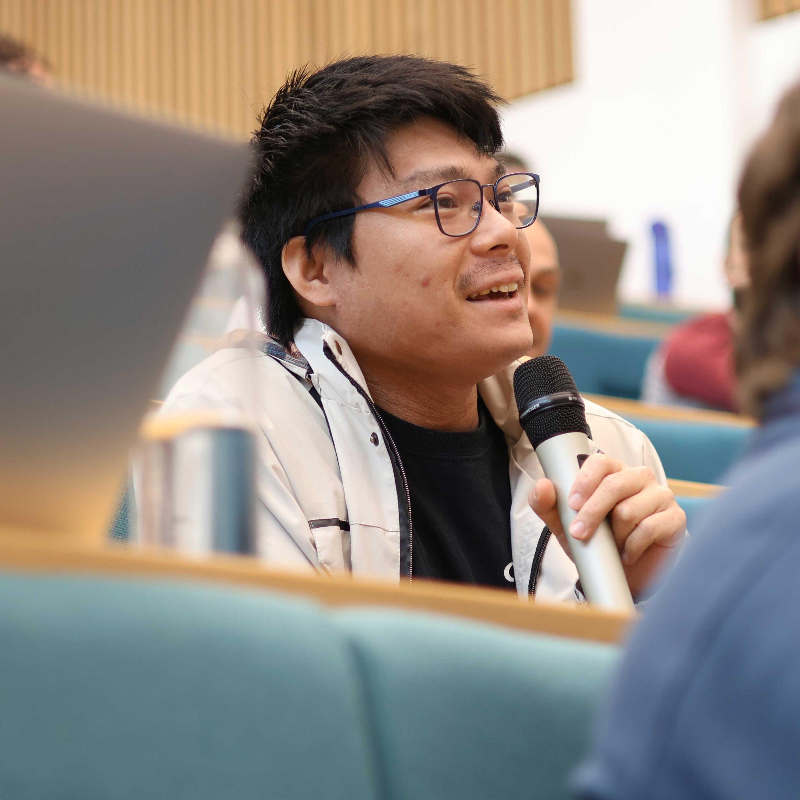 06 A person speaks into a microphone in a lecture theatre.