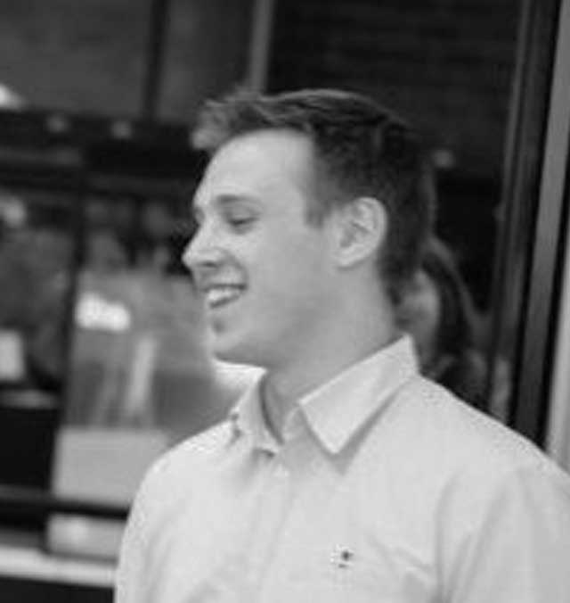 John-Hardy A black and white photo of John Hardy against a blurry background, smiling and looking to the left.