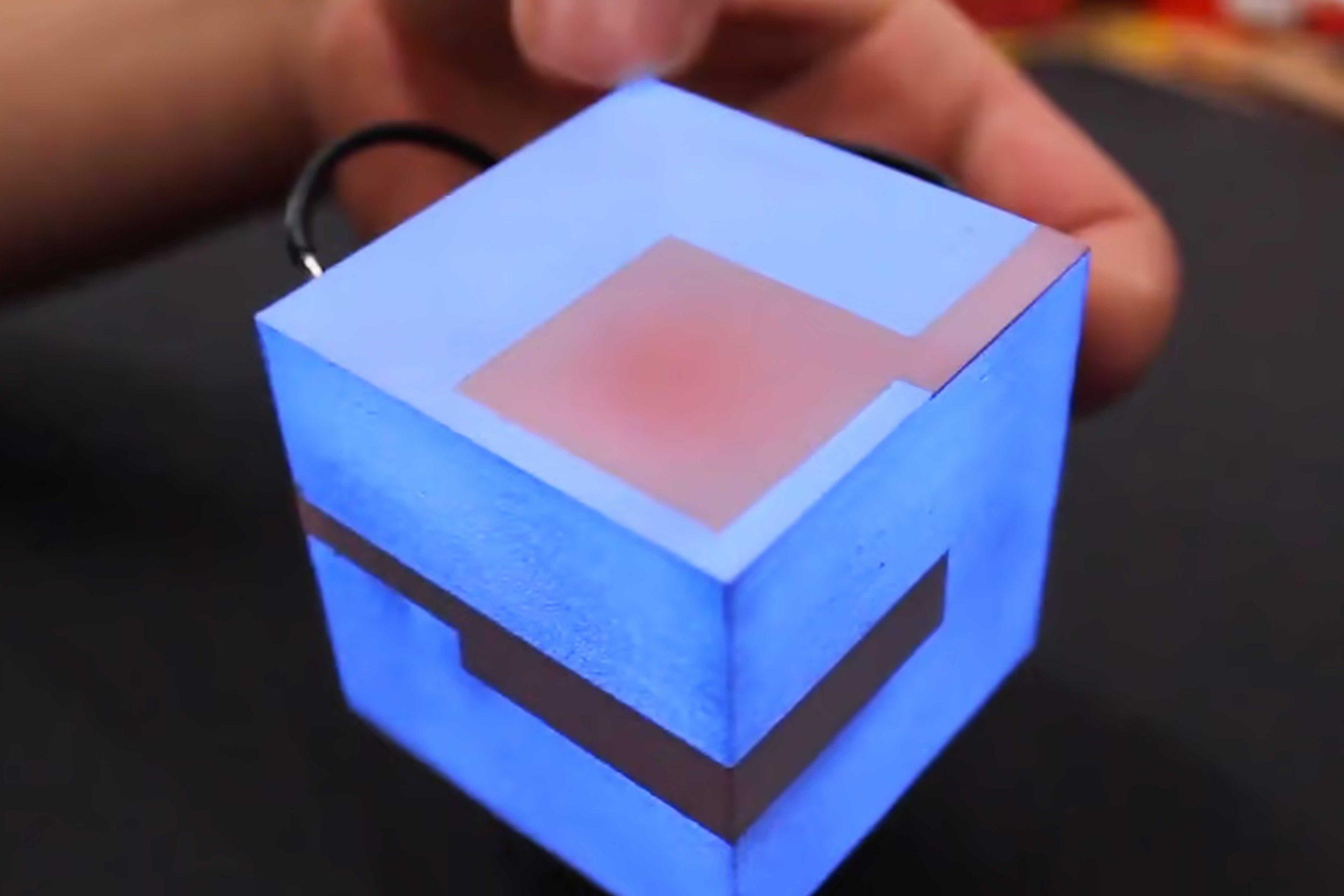 active_03 A close-up photo of a glowing blue cube with geometric patterns, which a person's hand is touching.