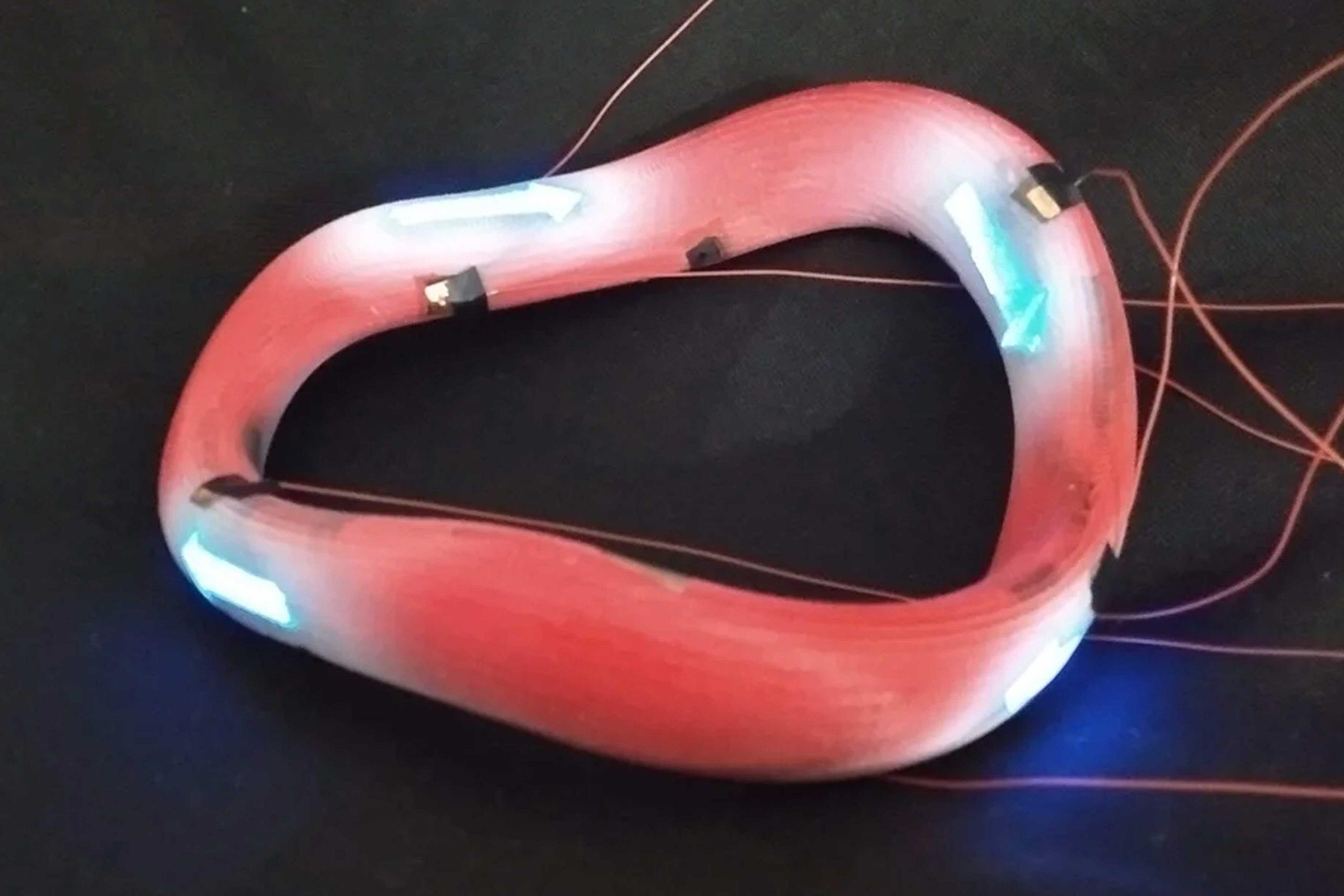 active_04 An oval ring with wires attached to it against a black surface. White arrows painted on it are glowing.