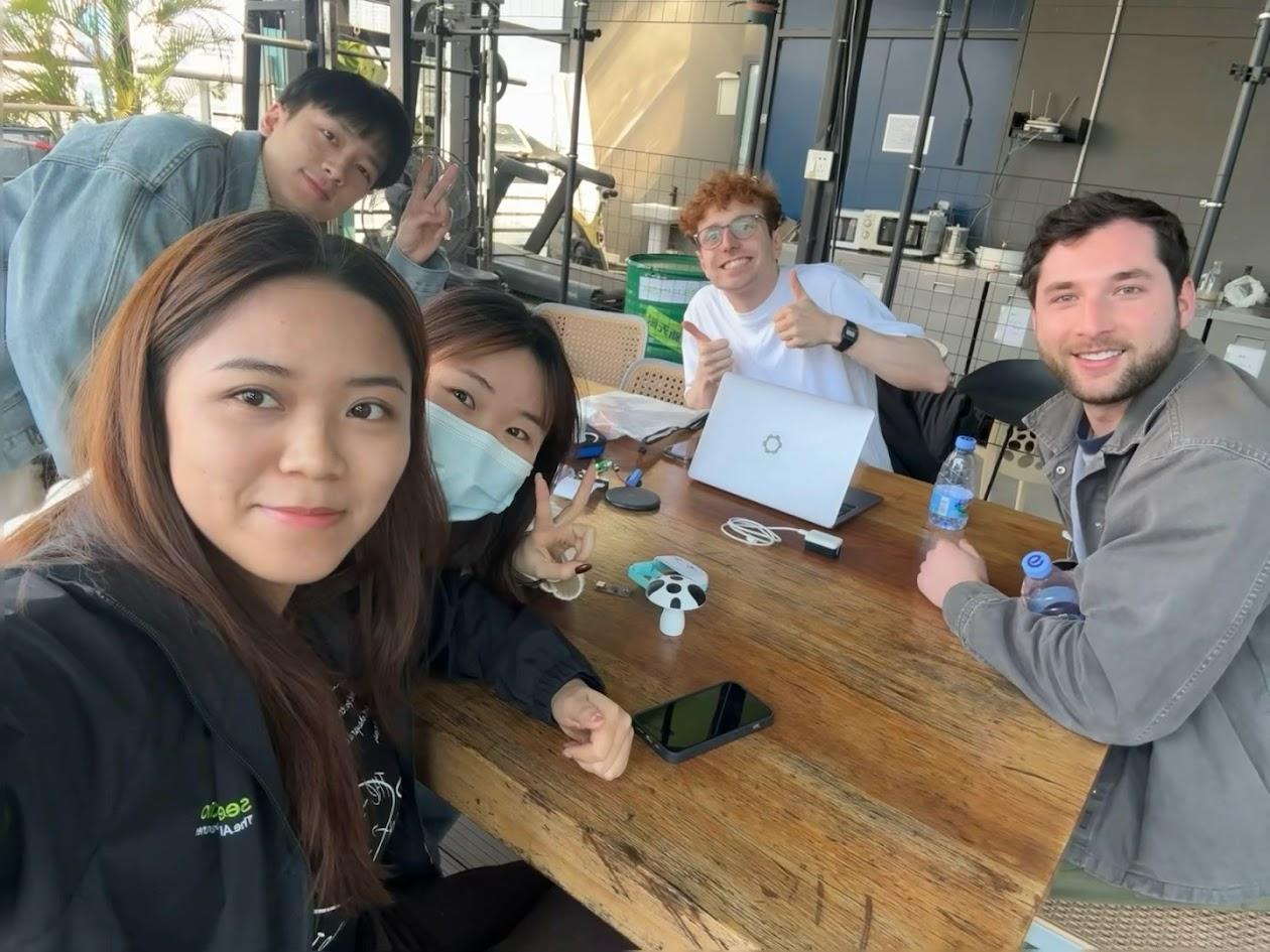 Seeed studio Oliver Child and his friend sit with a team of workers from Seeed Studio at the company's office. They are sitting around a wooden table with phones, a laptop and a device prototype.