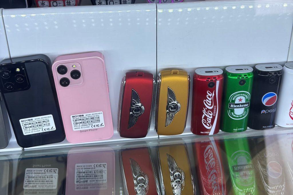Customised cell phones on display in a glass case. Some of them resemble beverage cans like Pepsi and Coca-Cola.