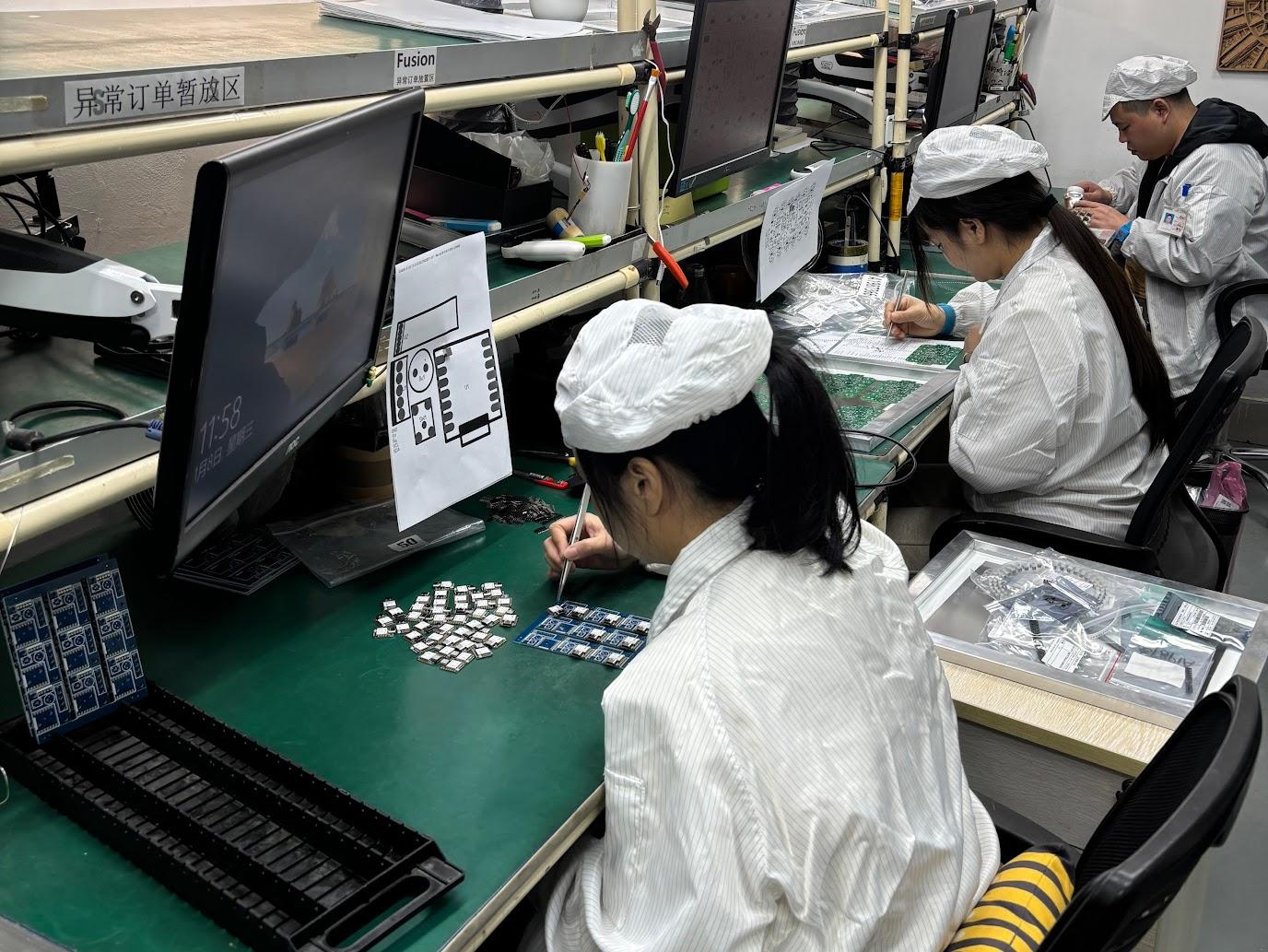 factory workers Workers wearing white lab coats and caps sit in front of desks assembling electronics
