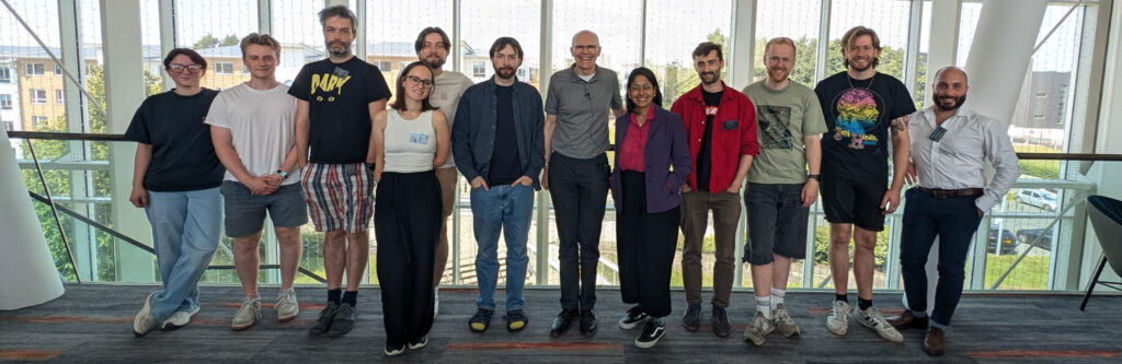Summer school prize winners stand in a row with event organiser Professor Steve Hodges in a Lancaster University building, with a large window behind them.